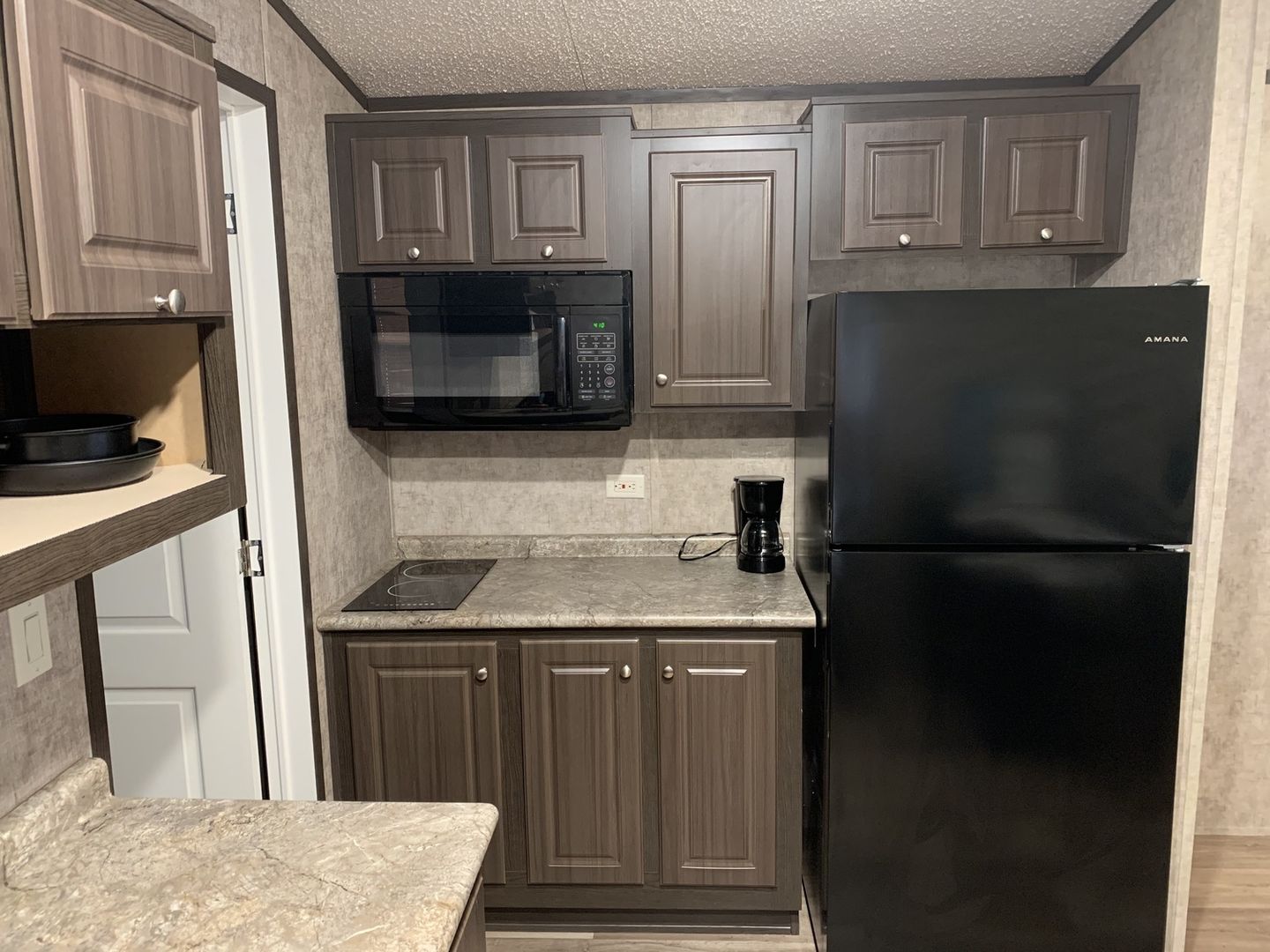 Tiny cabin kitchen with dark wood cabinets, a microwave and a black refrigerator.