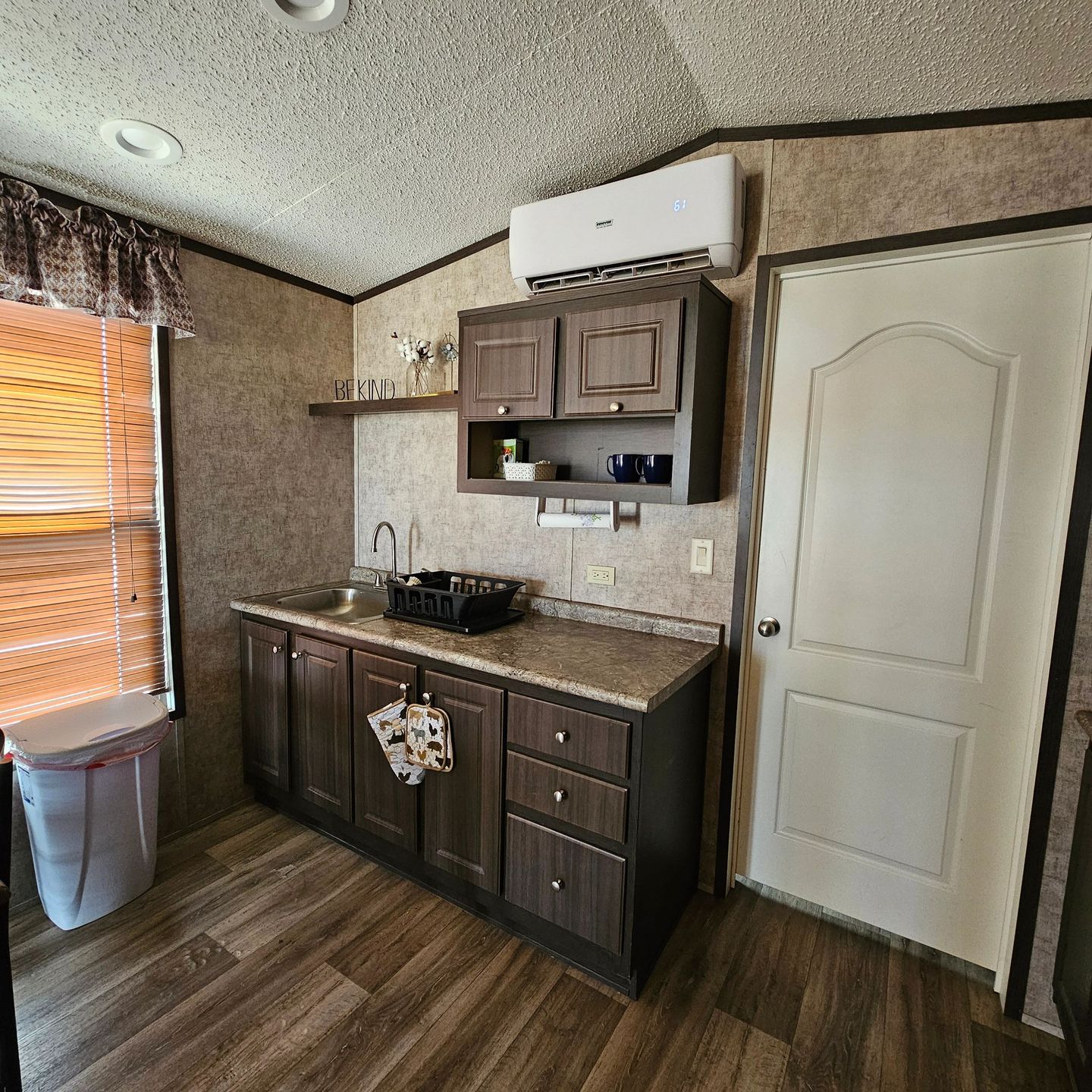 Tiny cabin sink, cabinets and open shelf beside a door.