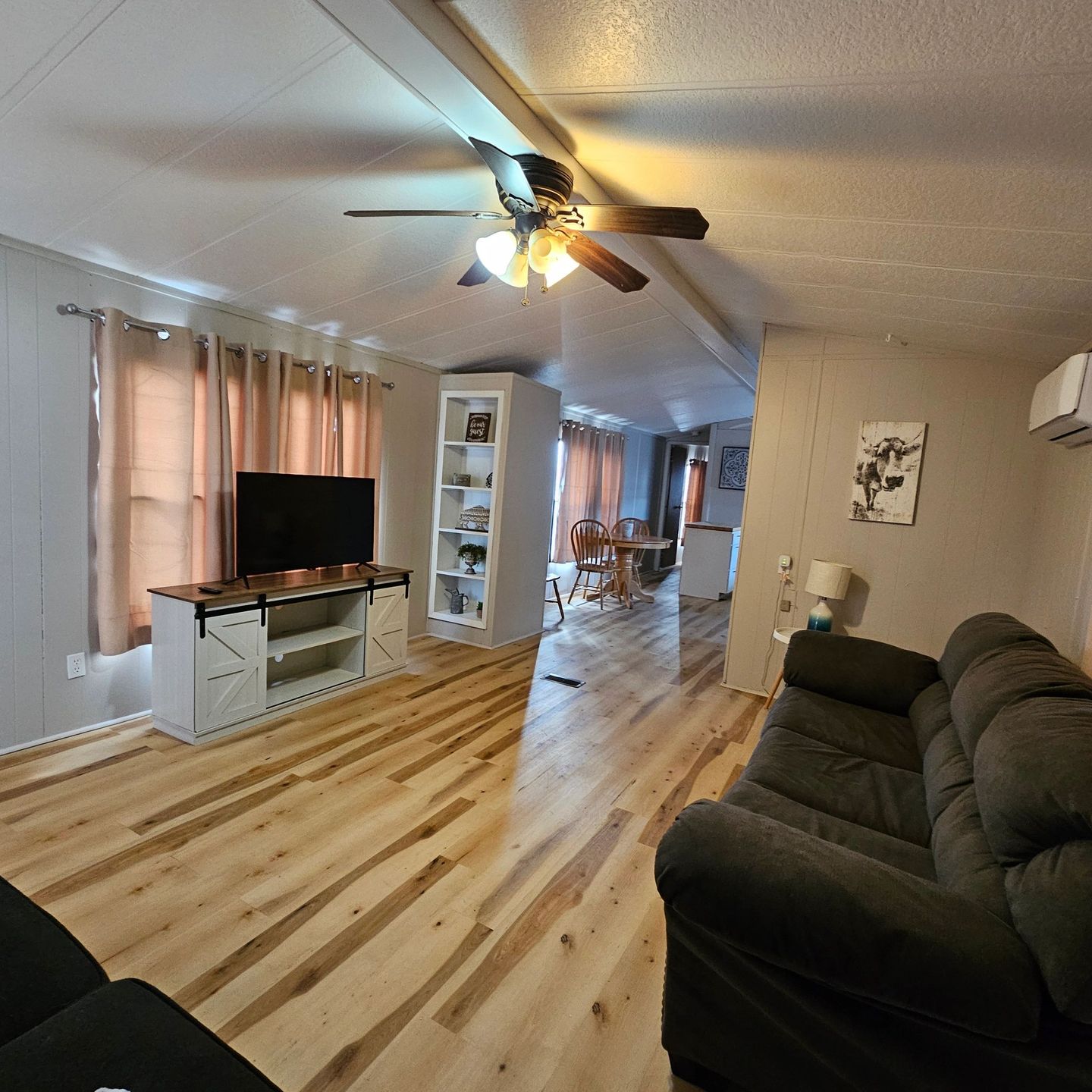 Guest house living room with plank floors, a sofa, a TV stand and a ceiling fan.