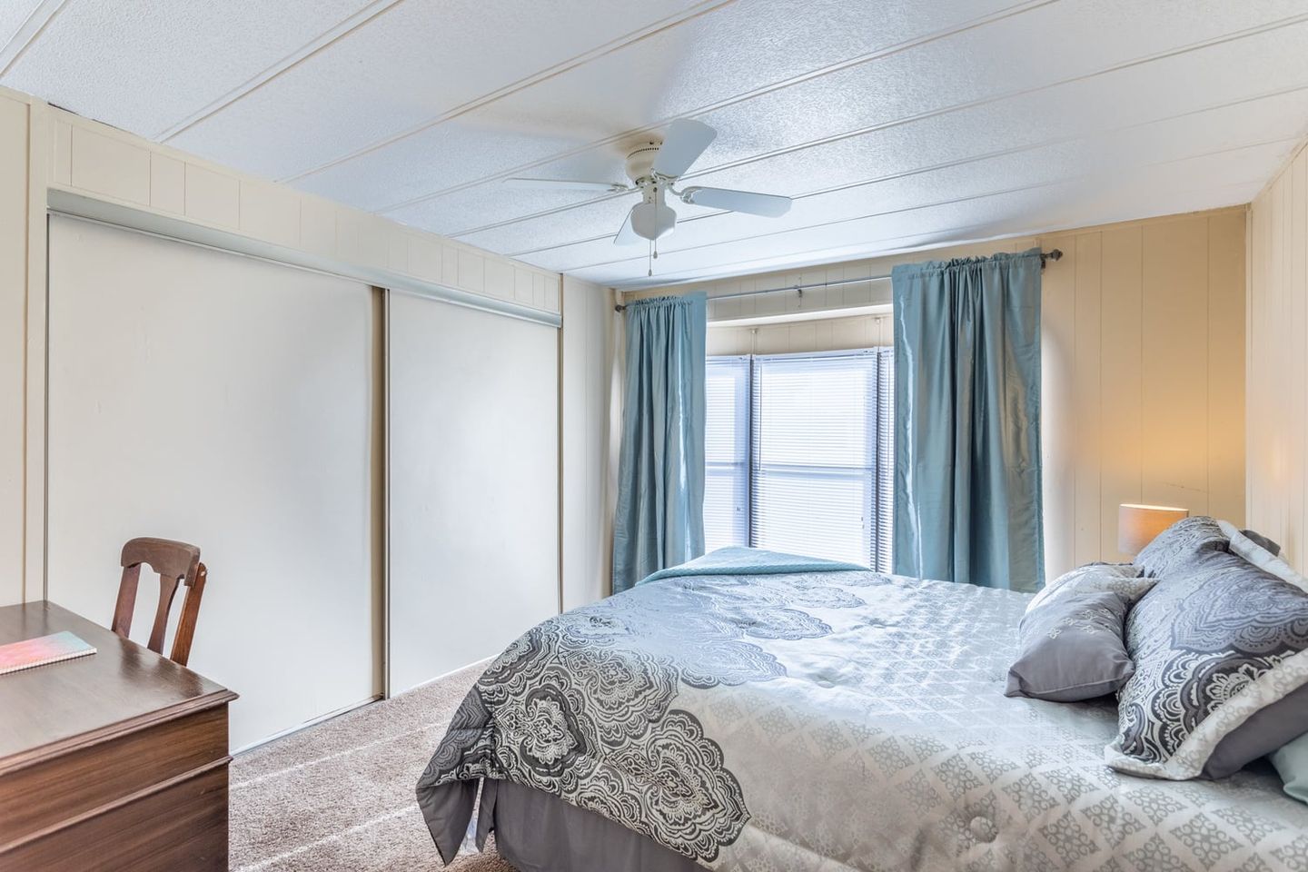 Guest house bedroom with a gray bedspread and teal curtains.