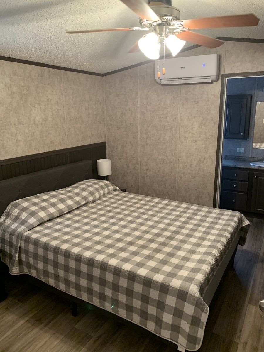 Tiny cabin bedroom with a checked bedspread and a ceiling fan.